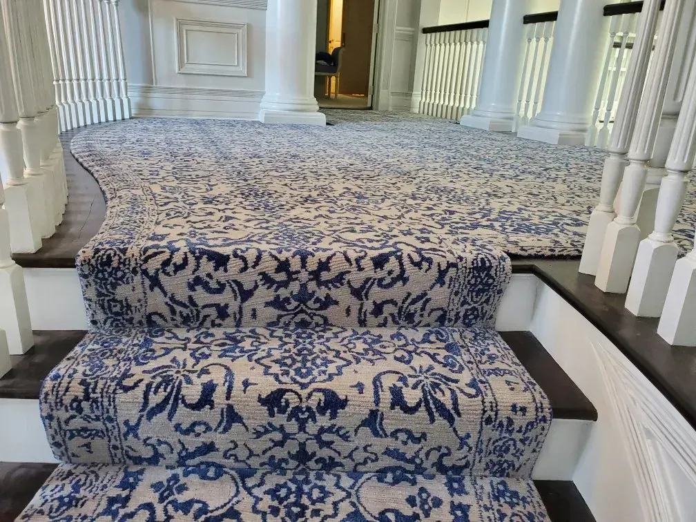 Blue and white patterned rug covers staircase and hallway with white columns and railing.