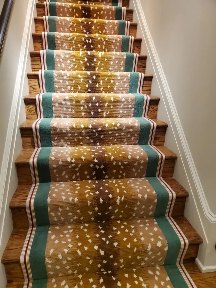 Staircase with wooden steps and a carpet runner with a deer spot pattern, bordered by green and red stripes.