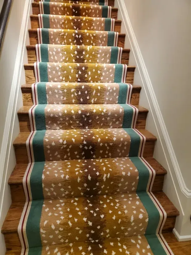 Staircase with wooden steps and a carpet runner with a deer spot pattern, bordered by green and red stripes.