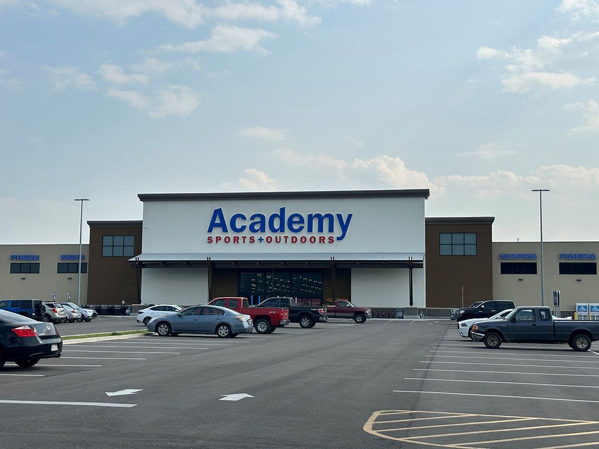 A academy store with cars parked in front of it.