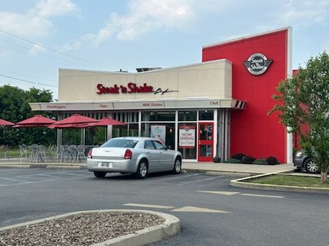A car is parked in front of a beige and red establishment