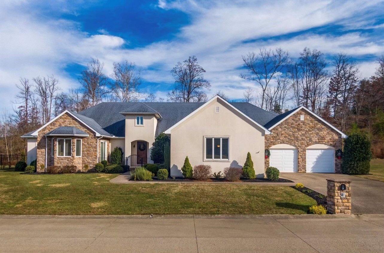 A large white house with two garages is sitting on top of a lush green hillside.