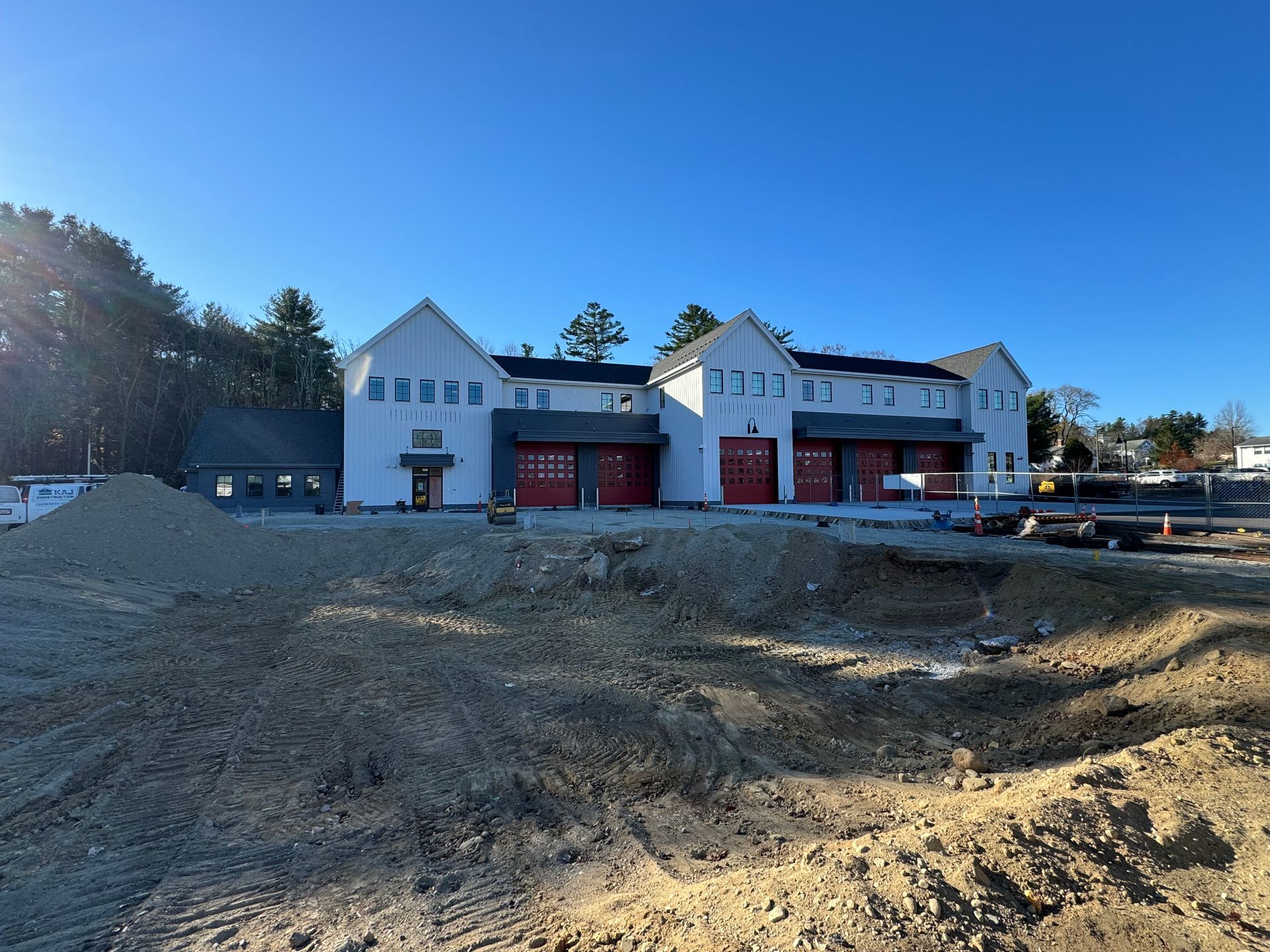 A large white building with red garage doors is being built in a dirt field.