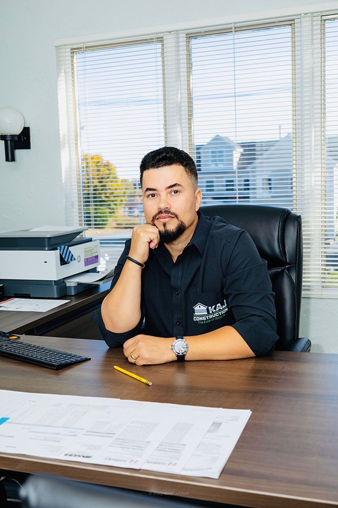 A man with a beard is sitting at a desk in front of a window