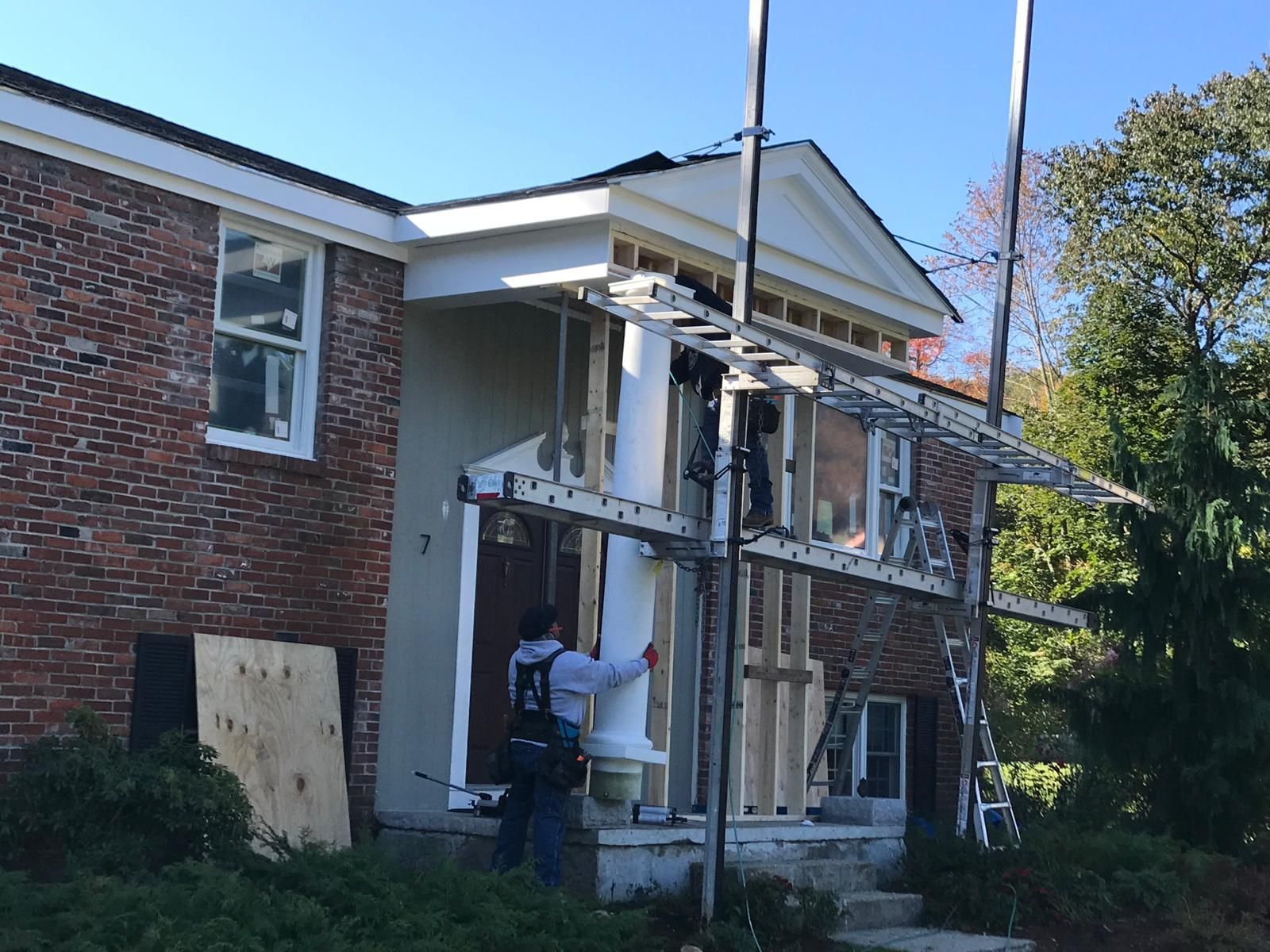 A man is standing on a ladder in front of a brick house.