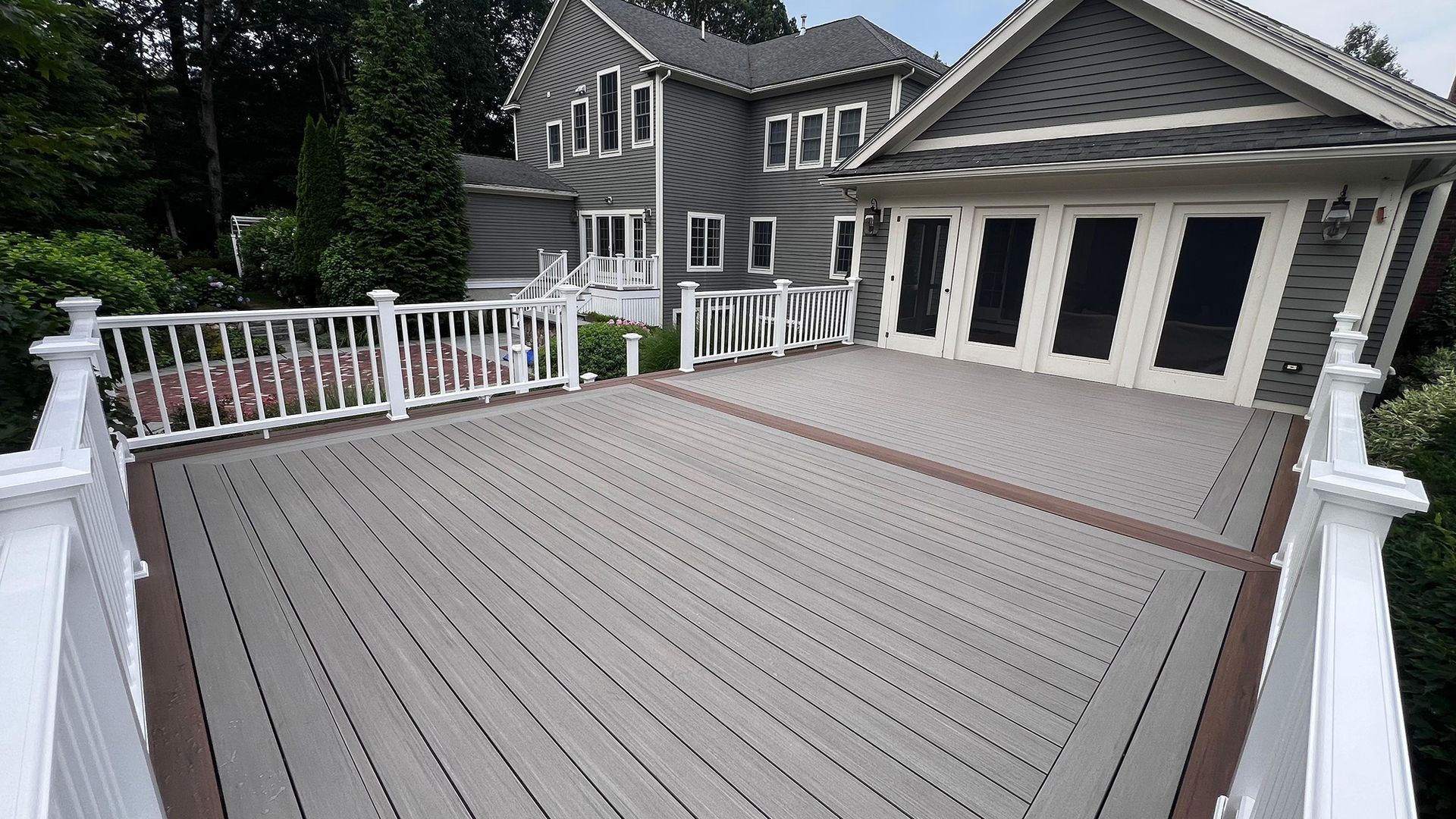 Gray deck with white railing, attached to a two-story gray house with large windows.