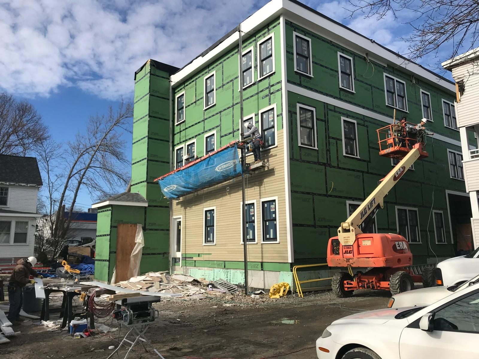 A large green building is being built with a white car parked in front of it.