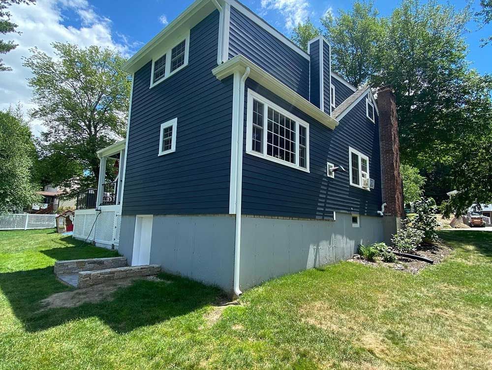A house with a blue siding and white trim is sitting on top of a lush green lawn.