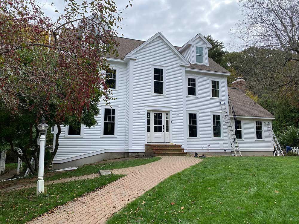 A large white house with a brick walkway leading to it is being painted.