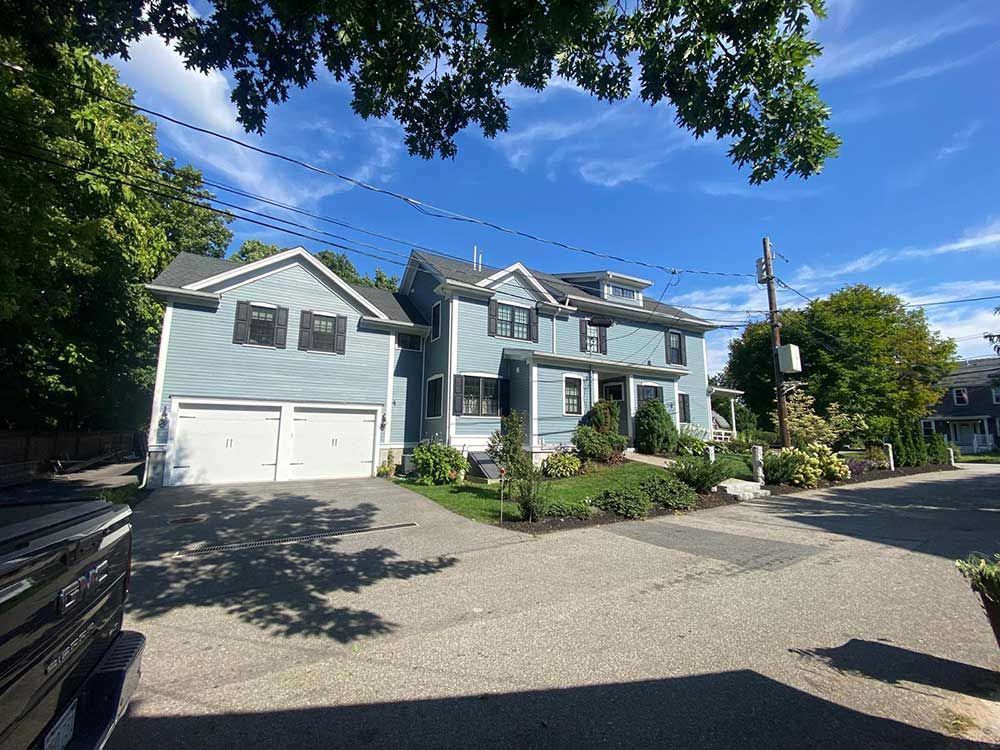 A blue house with a white garage and a black truck parked in front of it.