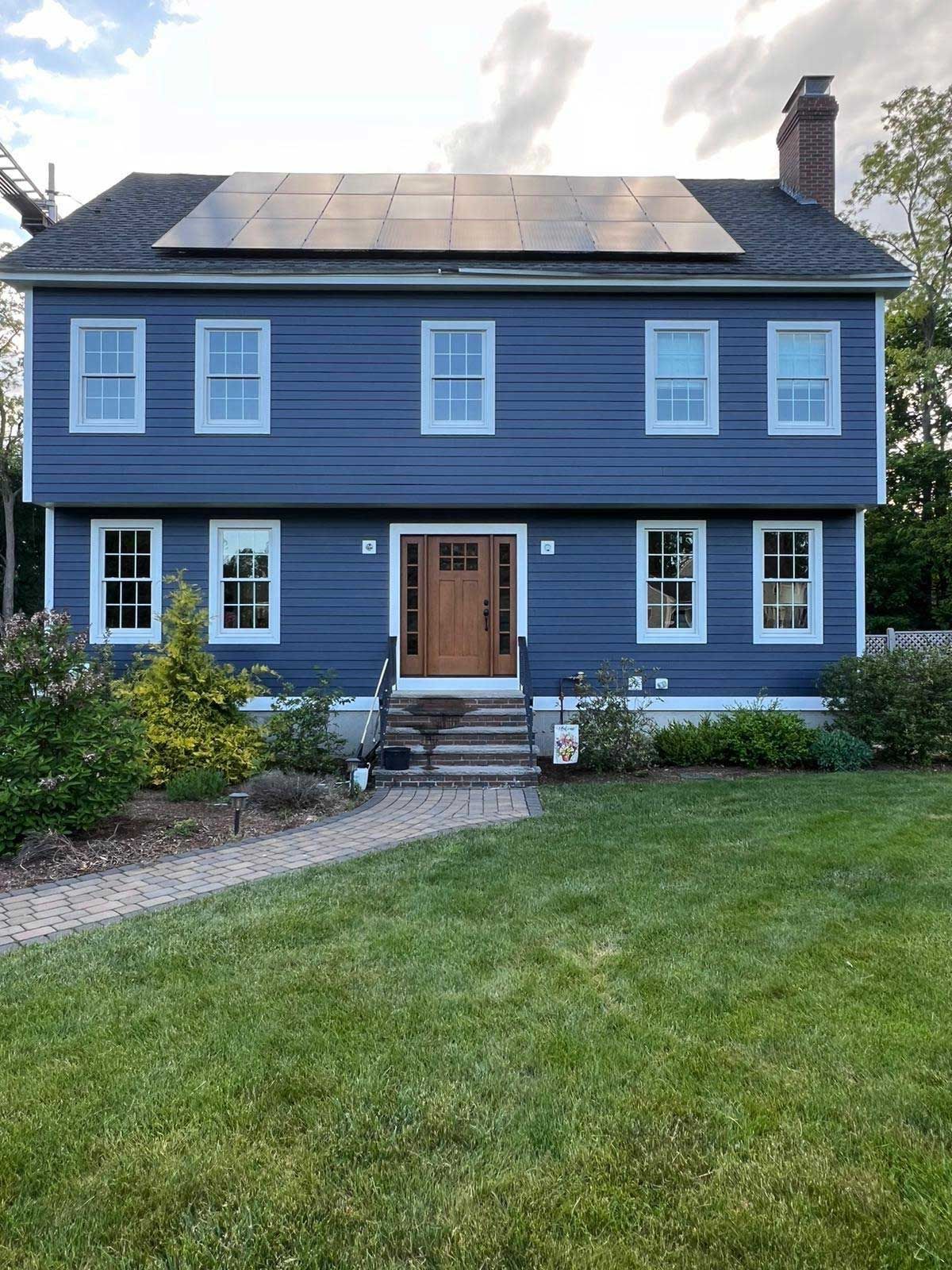 A blue house with solar panels on the roof is sitting on top of a lush green lawn.
