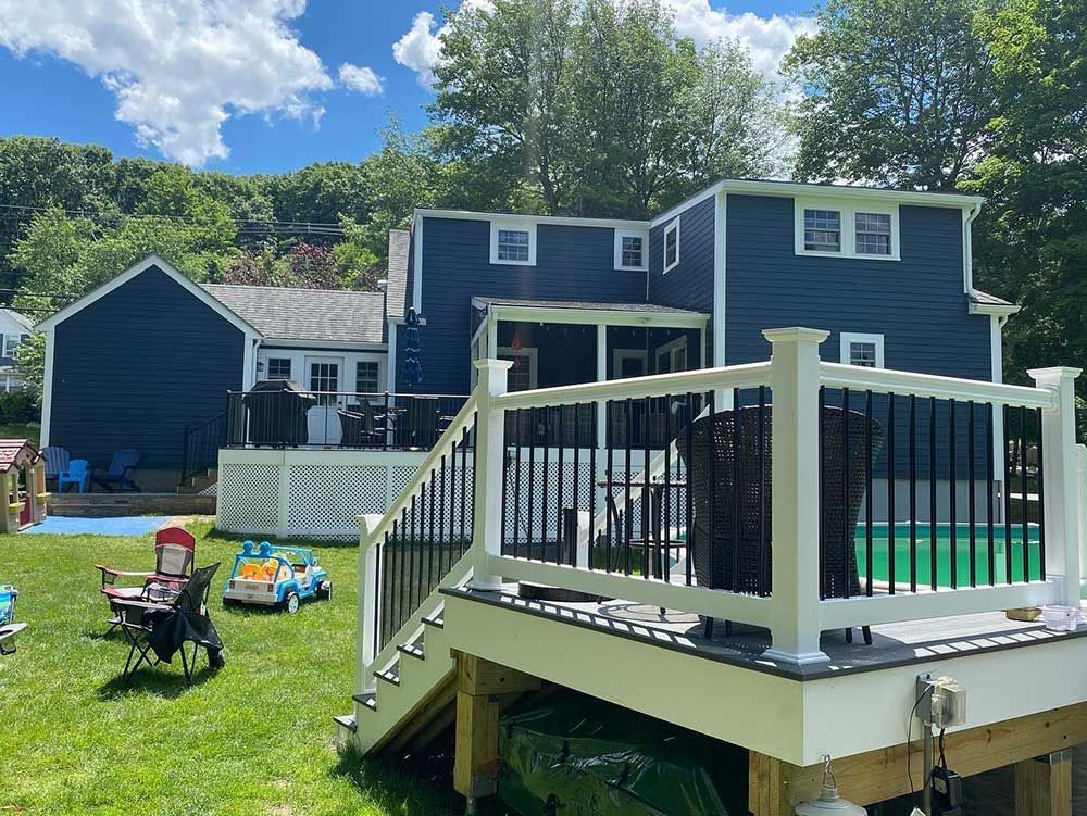 A large blue house with a white deck and a pool in the backyard.