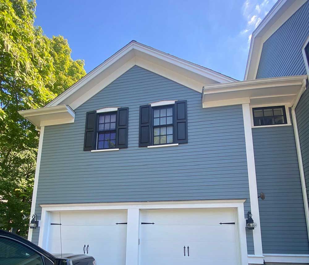 A car is parked in front of a blue house with black shutters