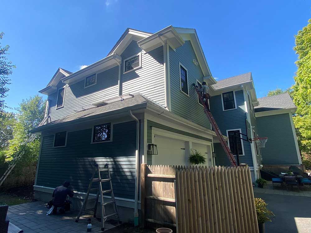 A man is painting the side of a house with a ladder.