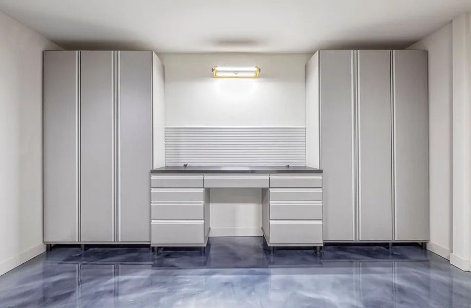 Garage workspace with gray cabinets, desk, metallic blue floor, and white walls.