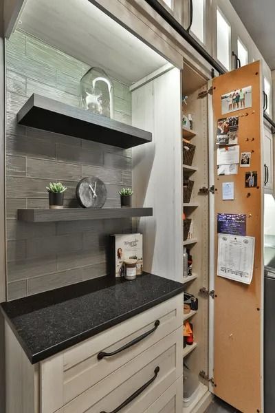 Pantry with floating shelves and sliding door revealing storage. Gray and white kitchen with dark countertop.
