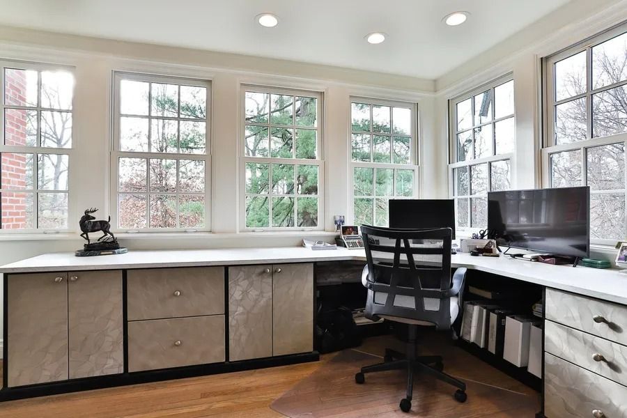 Home office with desk, computer, office chair, and windows overlooking trees.