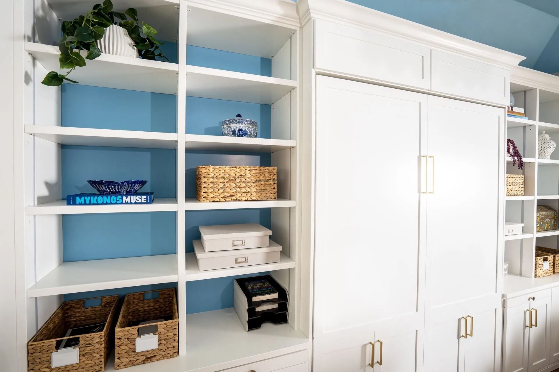 White built-in shelves with blue background, various decor items, and closed white cabinets with brass handles.