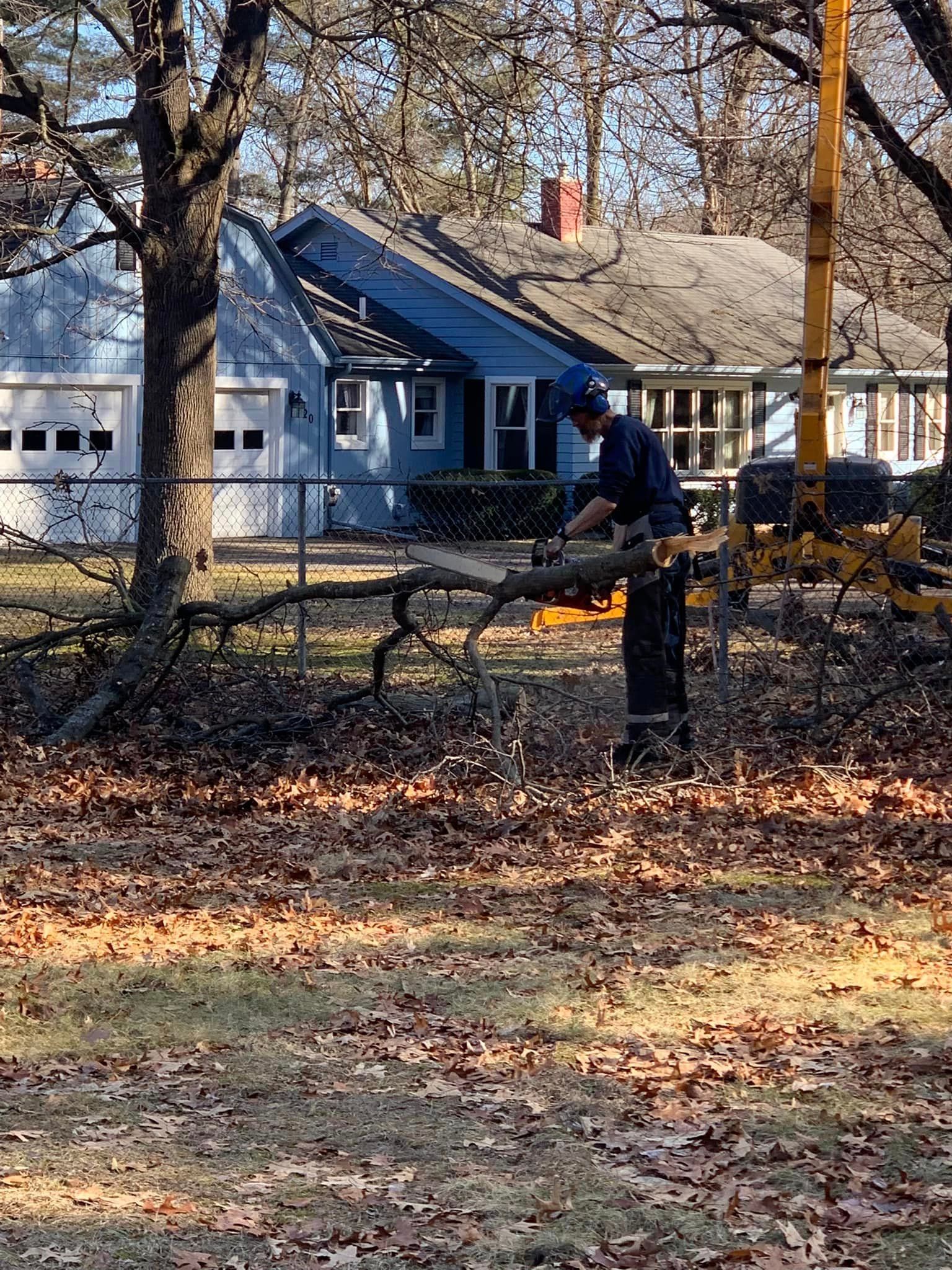 A man is cutting a tree branch with a chainsaw in front of a house.