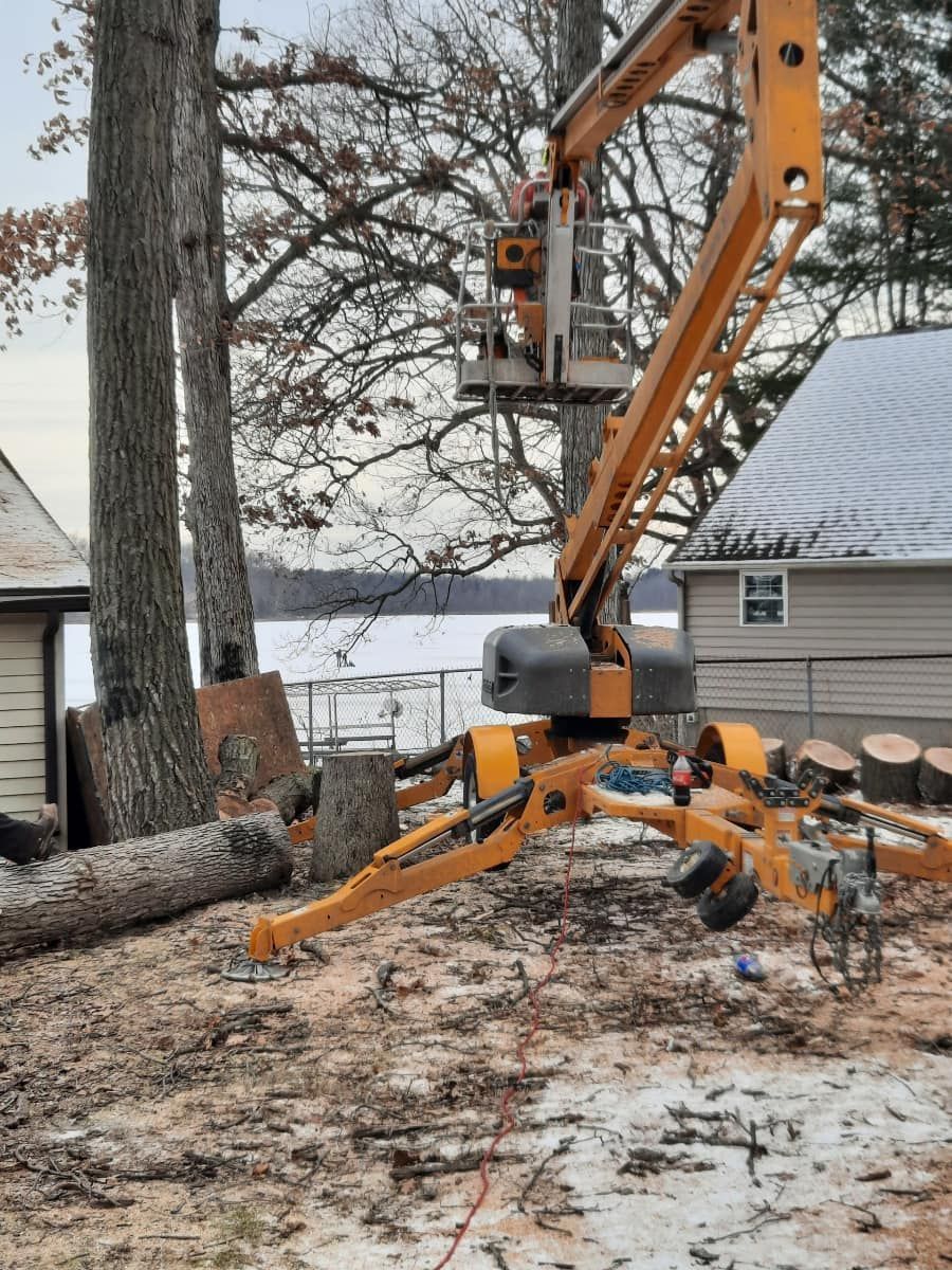 A crane is cutting a tree in front of a house