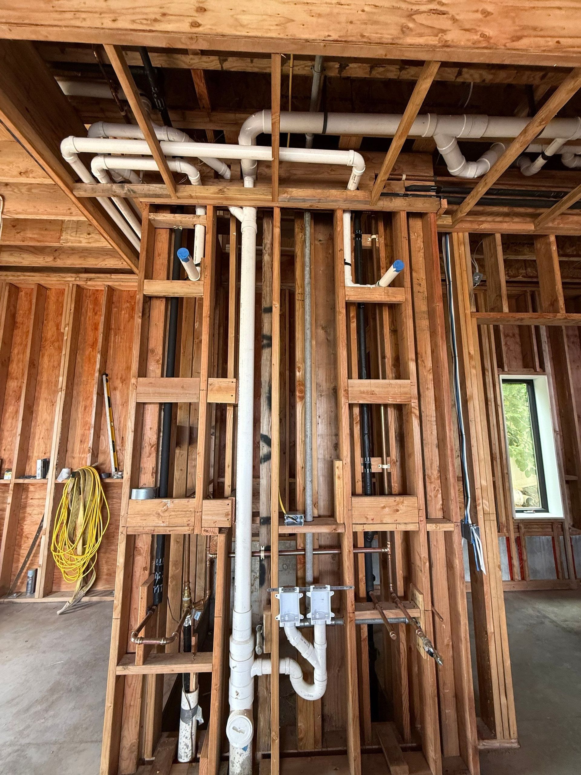 Exposed bathroom plumbing in unfinished wooden framing with pipes and valves near a window.
