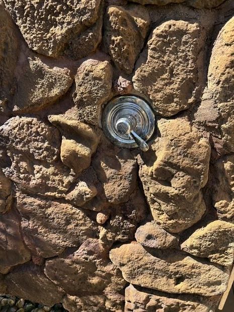 Showerhead mounted on a rustic stone wall, with a blue hose attached