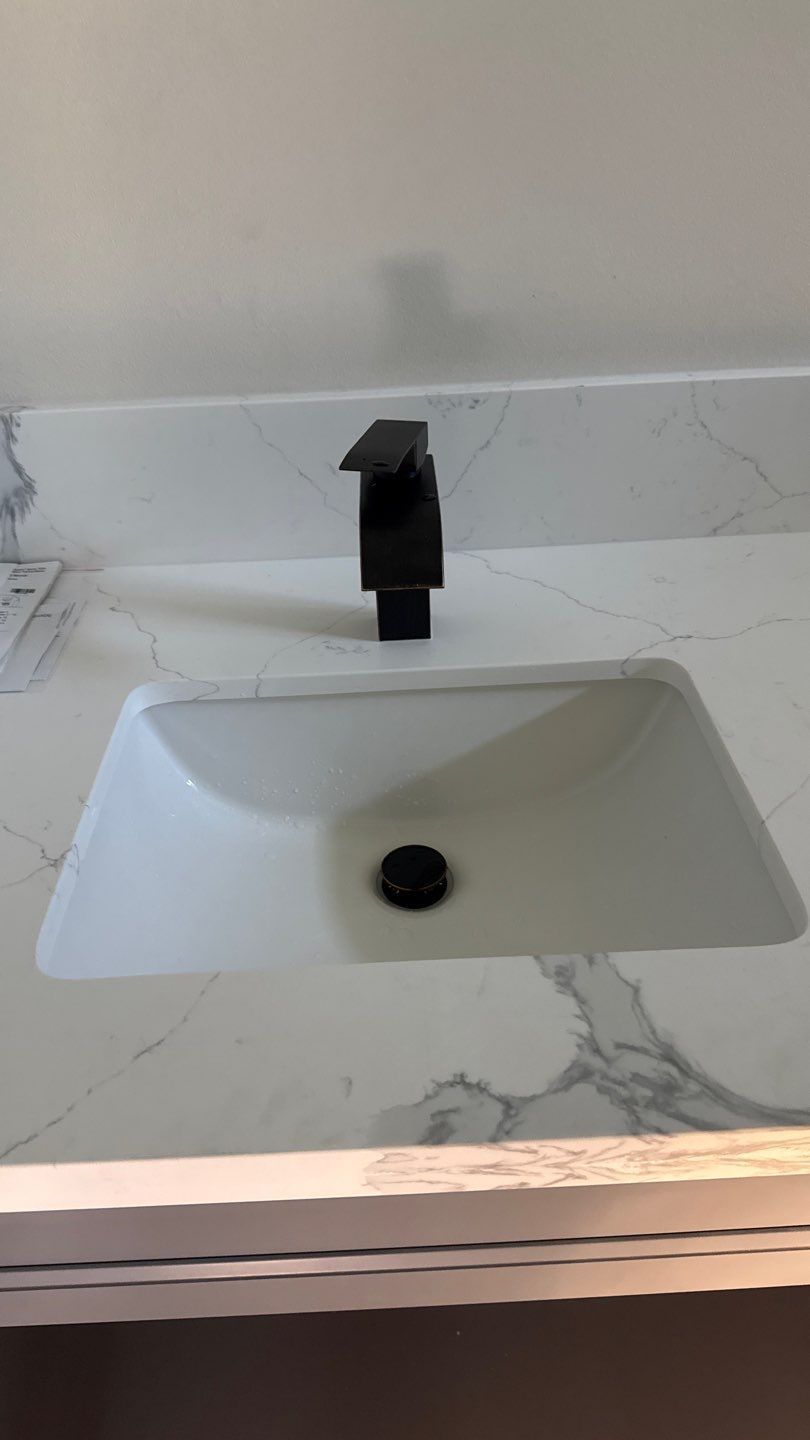 Modern white rectangular bathroom sink with black faucet on a marble countertop.