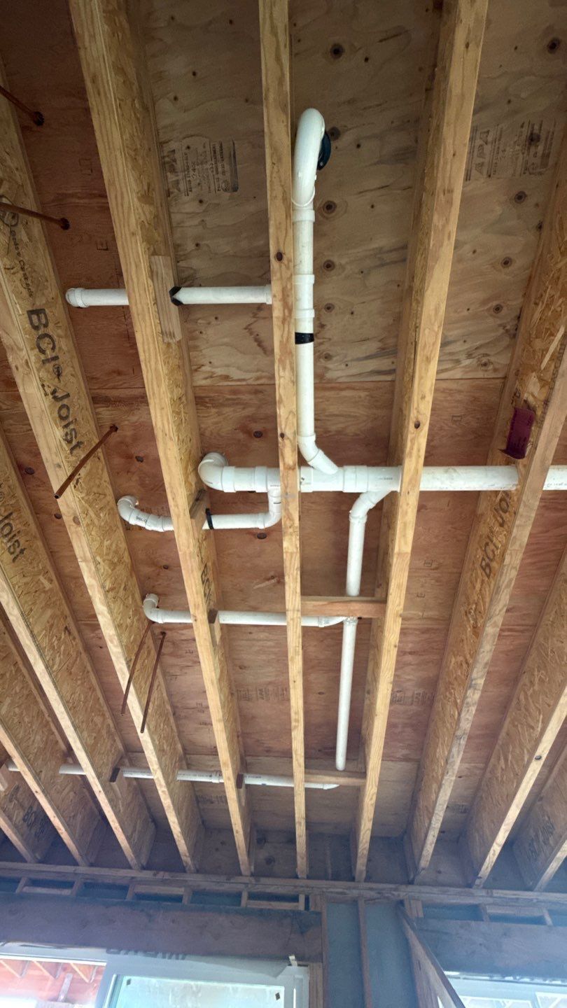 Exposed ceiling joists in a room with white PVC plumbing pipes running overhead