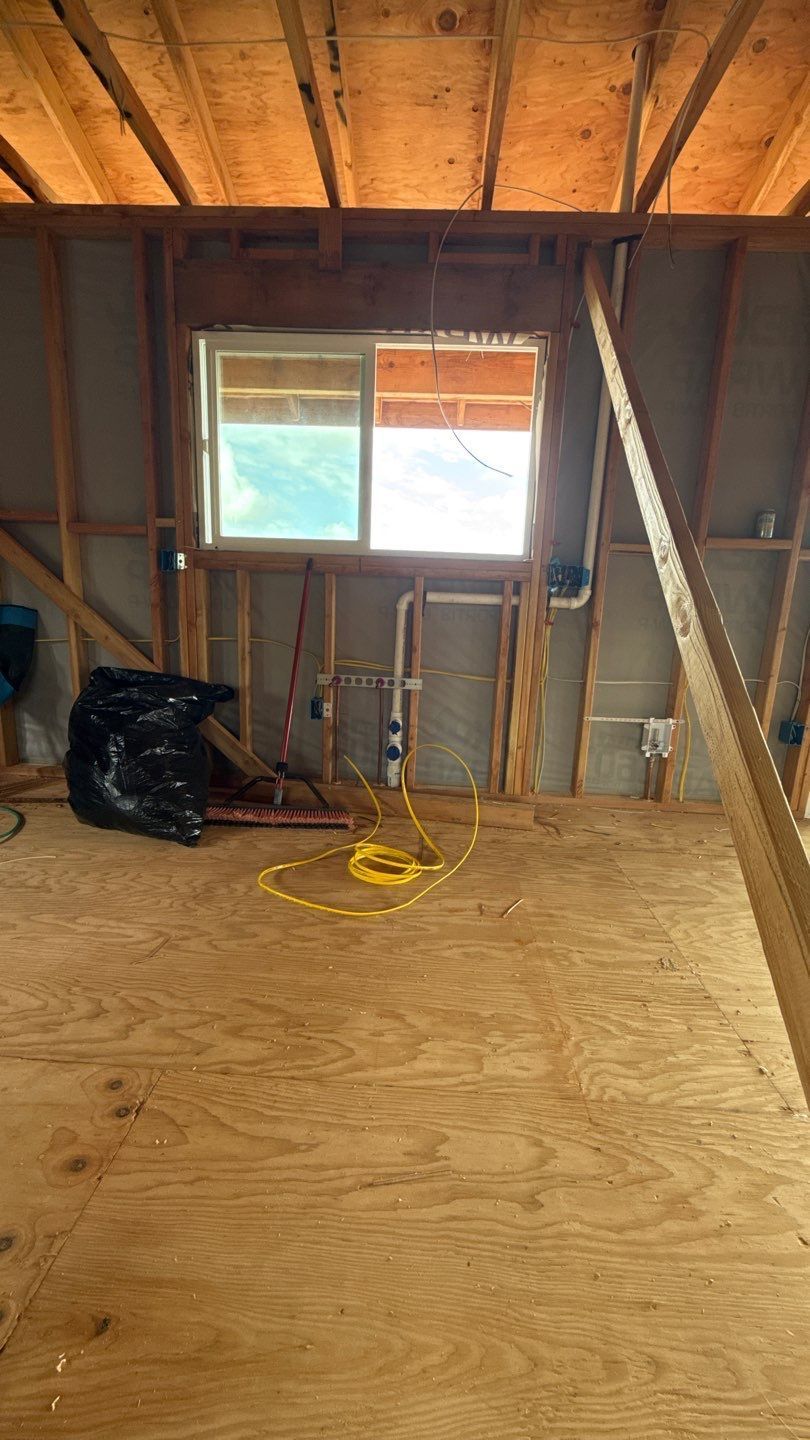 Unfinished attic room with plywood floor, exposed rafters, a window, and a black trash bag.