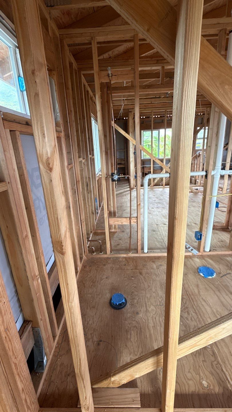 Unfinished wooden house framing with exposed studs and blue plumbing caps on the floor.