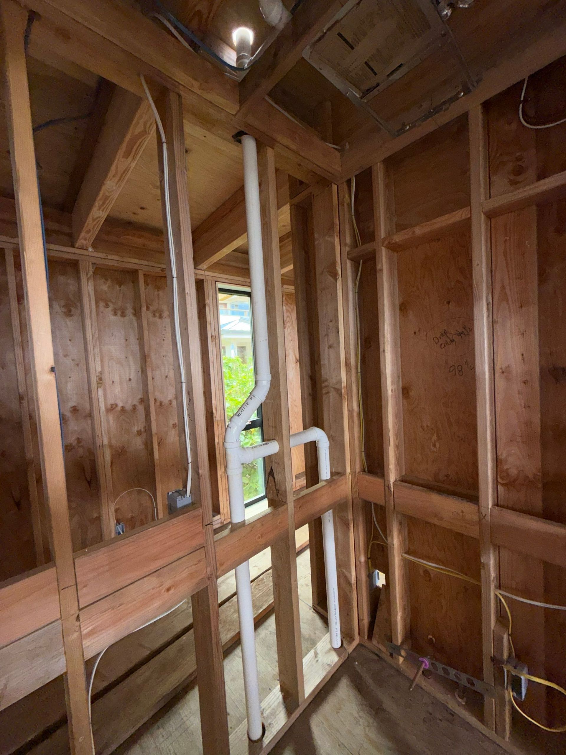 Bare wooden interior framing with a small window opening and exposed studs in a narrow unfinished room