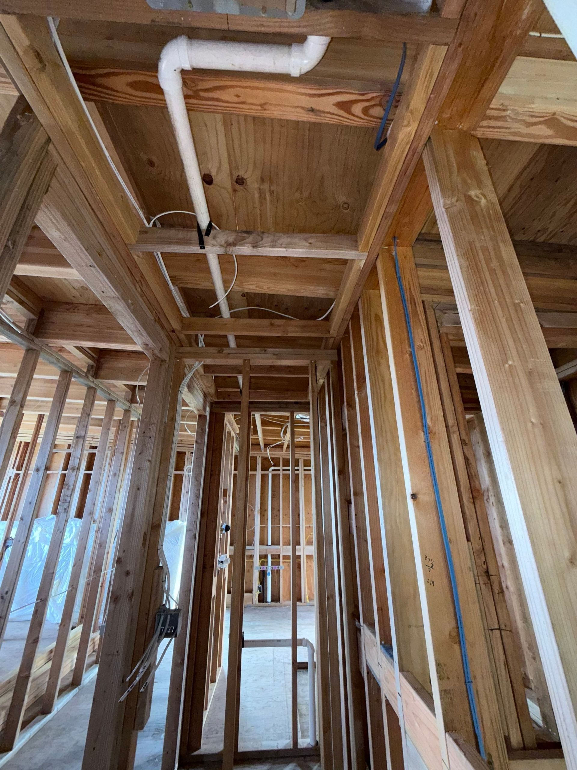 Interior of a wooden house under construction, showing exposed framing and plumbing pipes