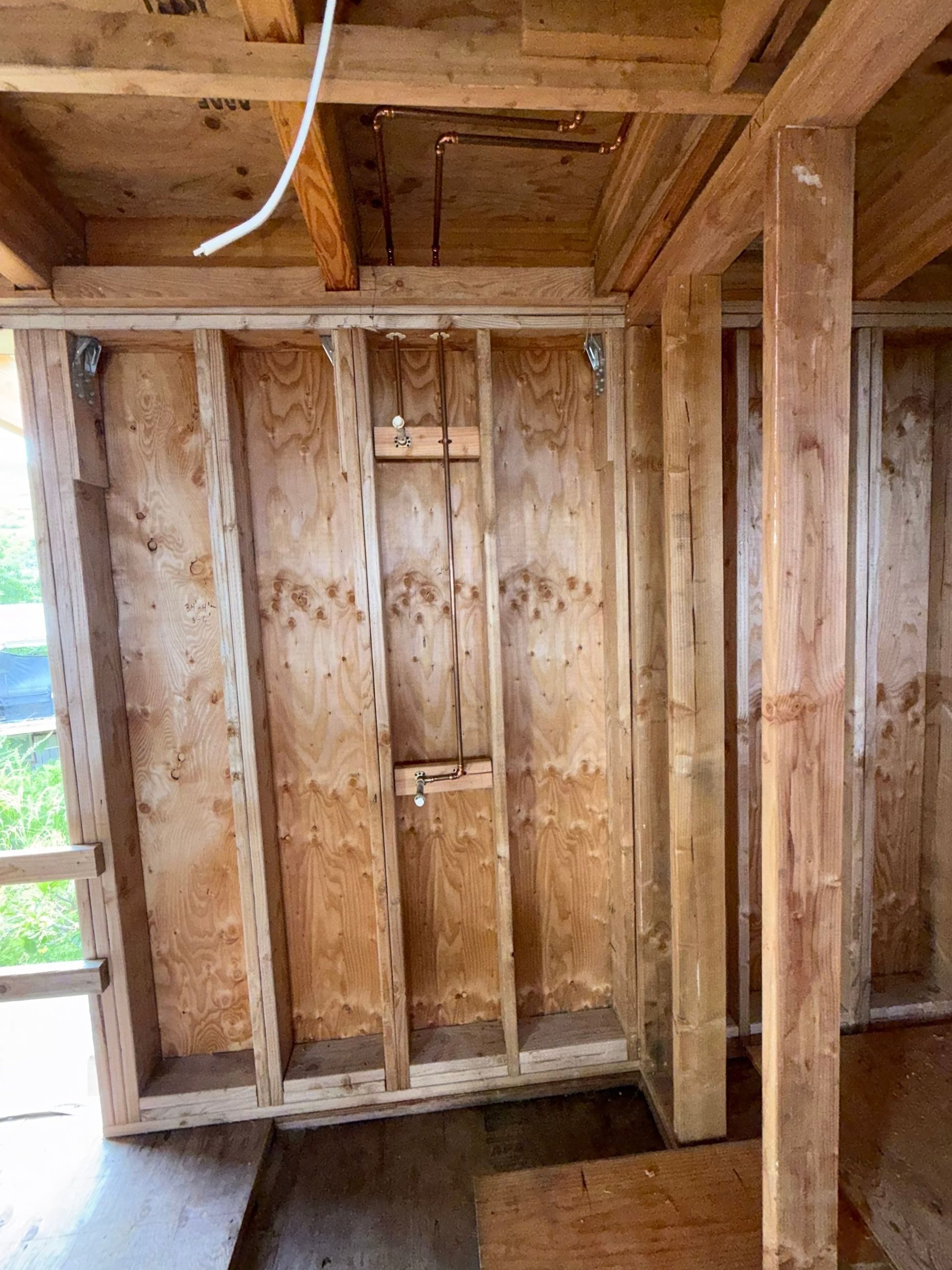 Unfinished wooden wall framing inside a house, with exposed studs and ceiling beams.
