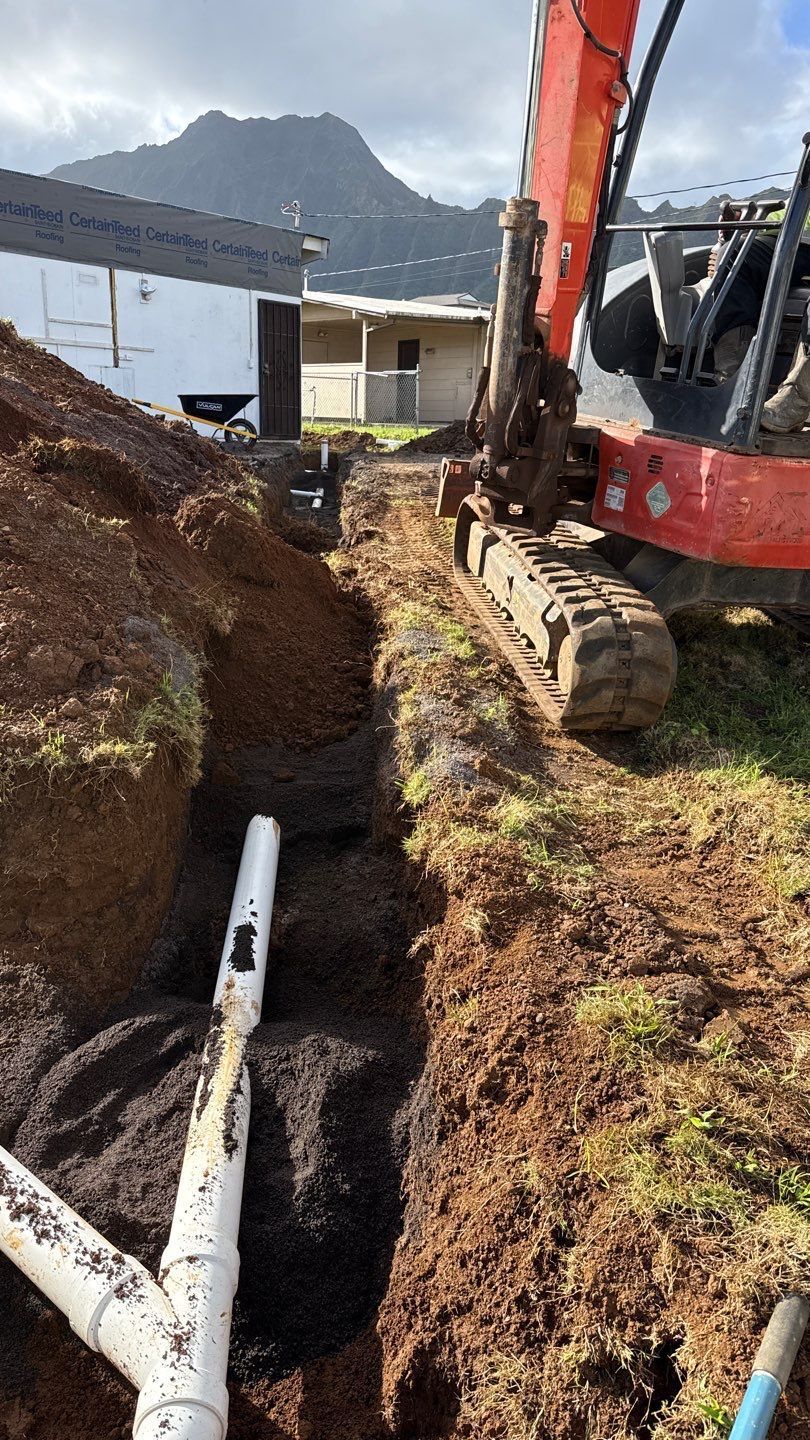 Excavator digging a trench beside white pipes at a construction site with a mountain in the background