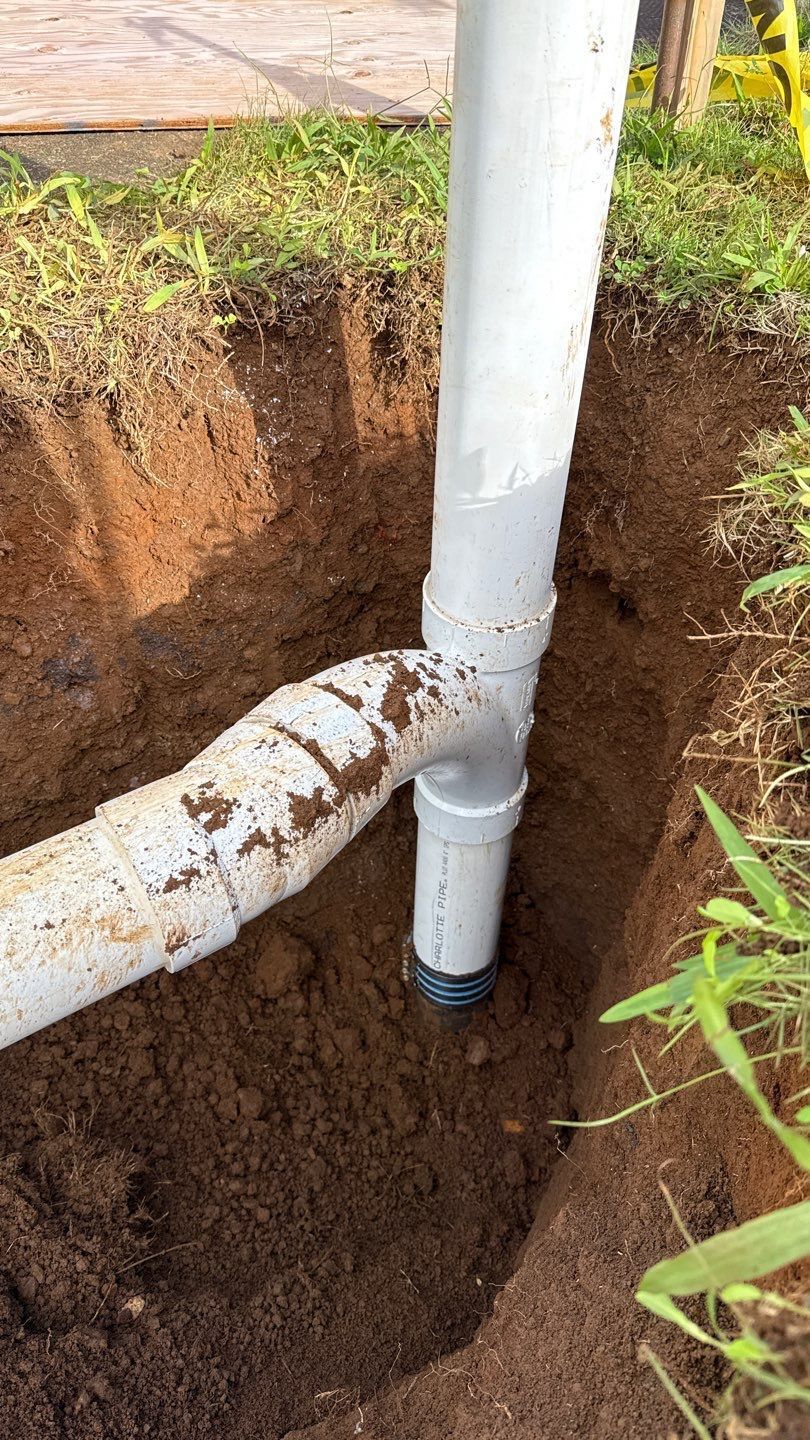 White PVC pipes in a dirt trench, with one horizontal pipe connected to a vertical pipe outdoors.