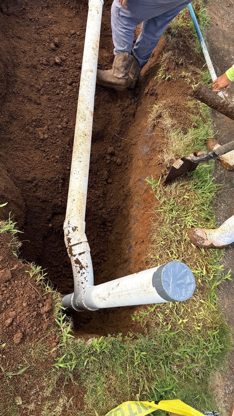 Workers digging a trench beside white drainage pipes and a capped pipe outdoors