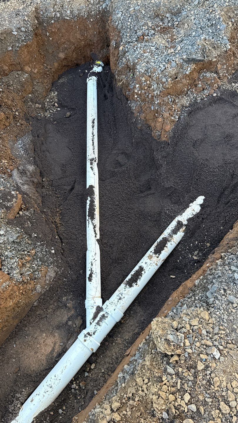White PVC pipes branching in a rocky dirt trench, forming a V shape.