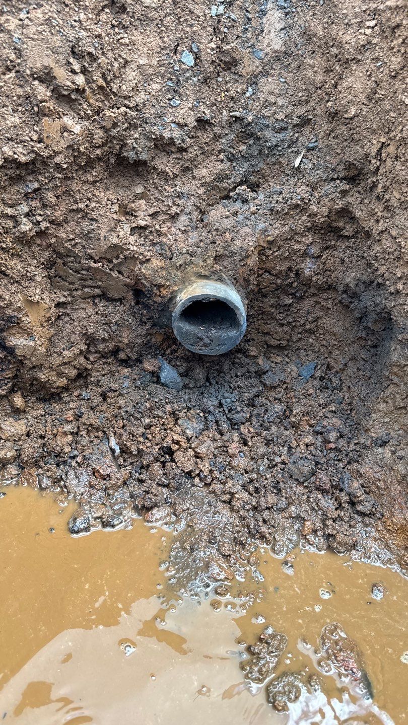 Small dark pipe opening in muddy dirt near a puddle of brown water