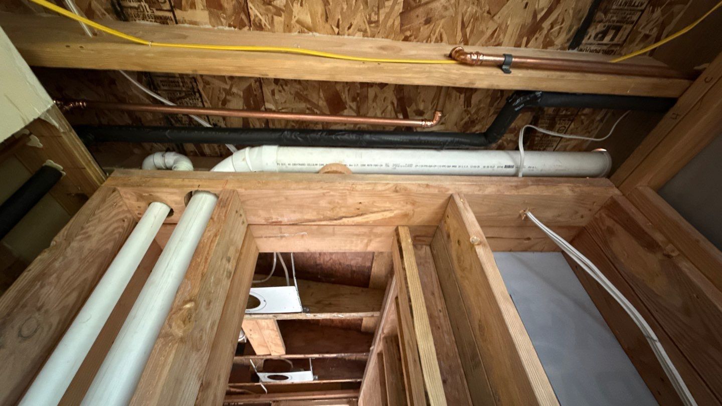 Exposed attic framing with insulation, white PVC pipes, and a central opening looking down into the floor below