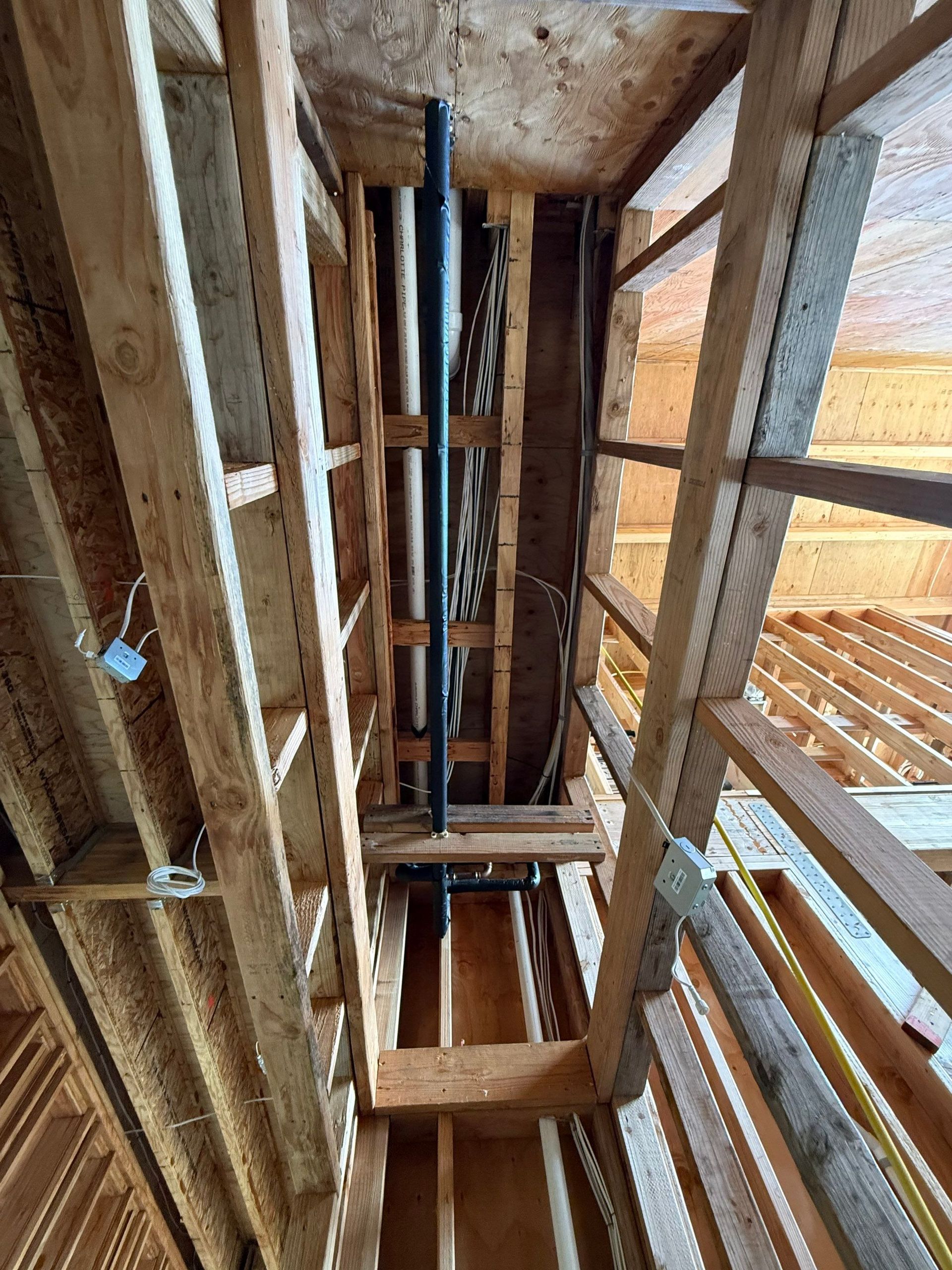 Construction ceiling with exposed wooden framing and vertical pipes in a narrow shaft.