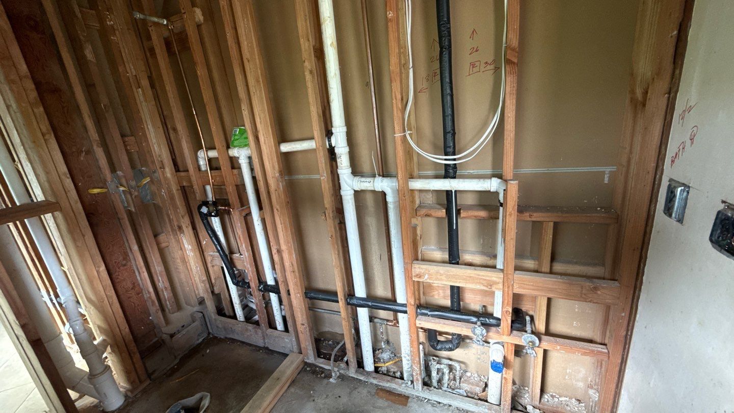 Exposed wall framing with plumbing pipes and electrical wiring in an unfinished room under renovation