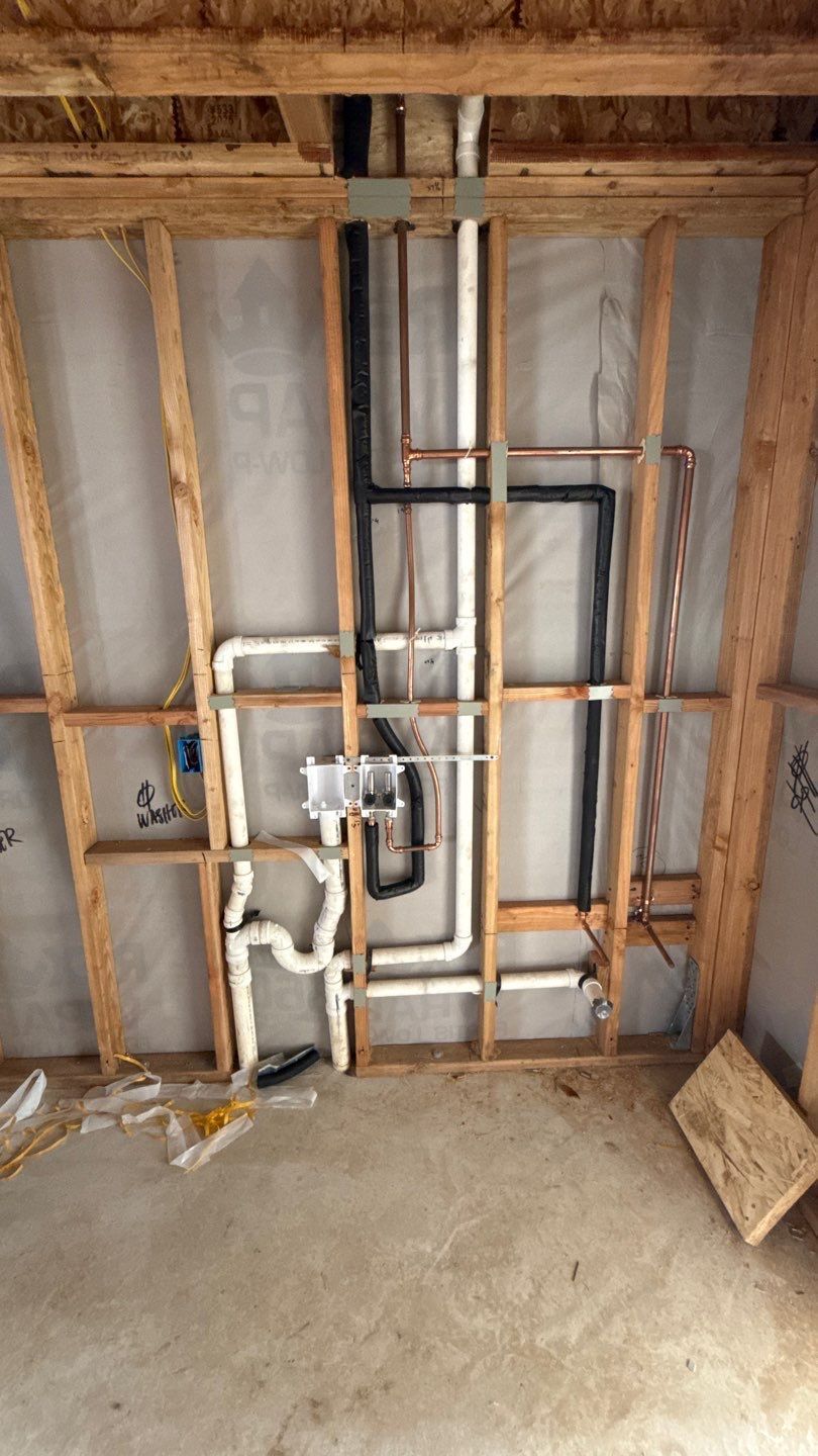 Exposed wall framing with plumbing and electrical pipes in an unfinished room under construction