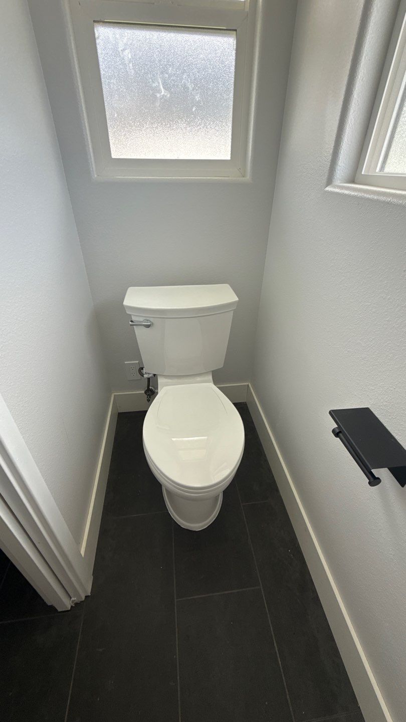 Small narrow bathroom with a white toilet, dark tile floor, and frosted window.