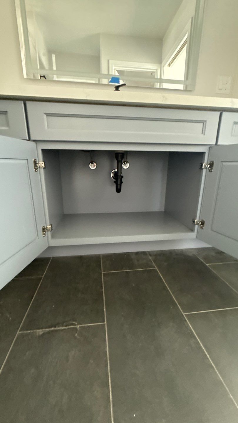 Open bathroom vanity cabinet with gray doors and visible plumbing under a sink.