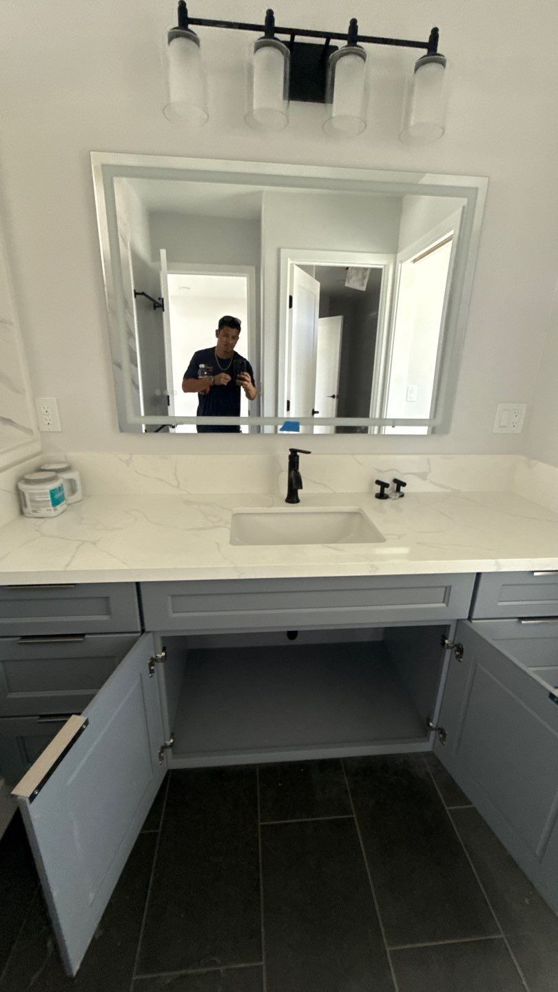 Bathroom vanity with large mirror, white sink, open gray cabinets, and a person reflected taking the photo