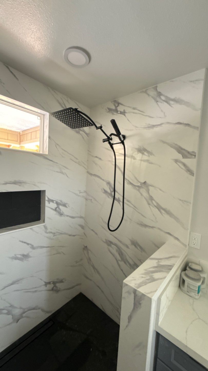 Tiled shower with black rainfall showerhead, handheld sprayer, and built-in niche shelf.
