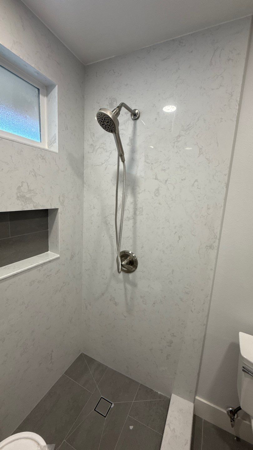 Shower stall with tiled walls, handheld showerhead, and wall niche in a small bathroom.