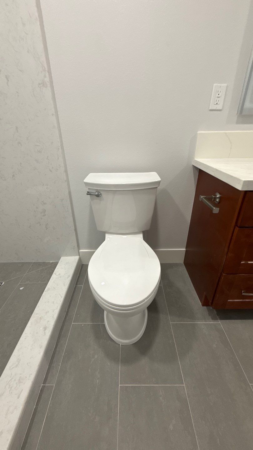 White toilet in a small bathroom with gray tile floor and brown vanity sink on the right.