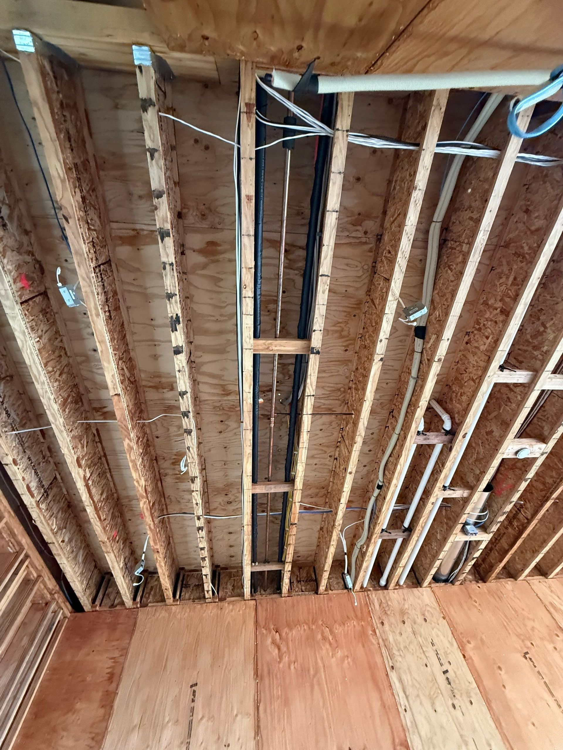 Exposed wooden ceiling joists with insulation and wiring above a paneled wall