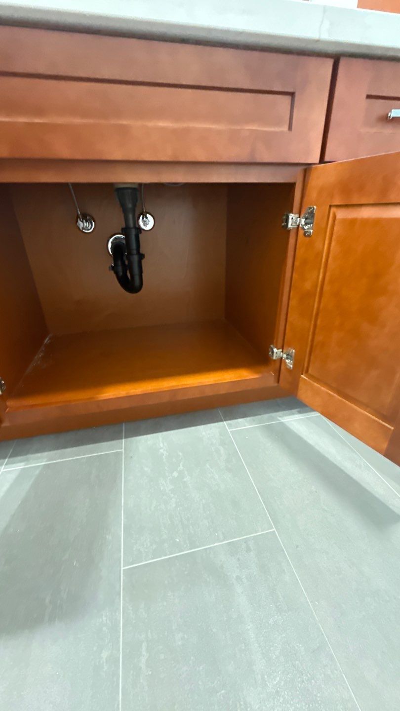 Open wooden bathroom vanity cabinet with black plumbing and gray tile floor.